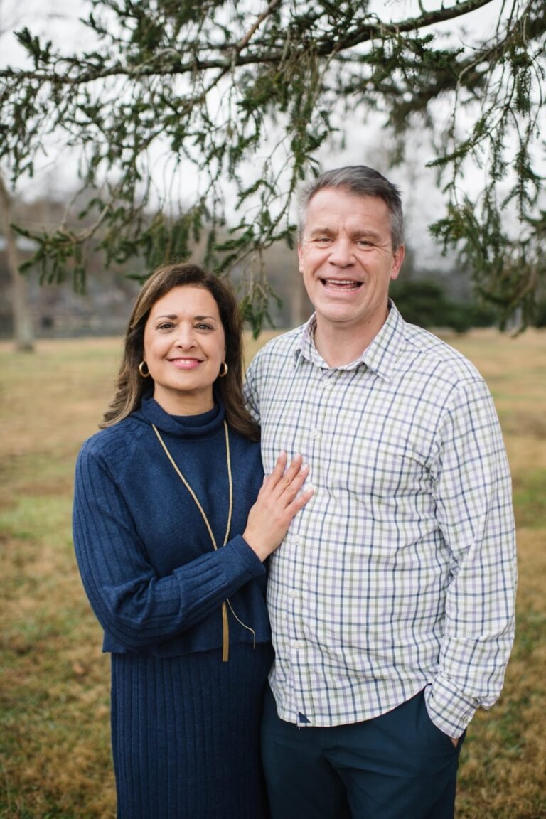 John and Stephanie Case standing together outdoors beneath an evergreen tree